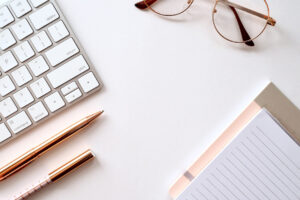 office desk with keyboard, pens, glasses and notepad